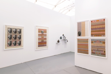 Installation view of an art fair booth. Sculptures and collages are on the walls