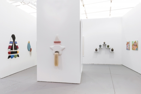 Installation view of an art fair booth. Sculptures and paintings are on the walls
