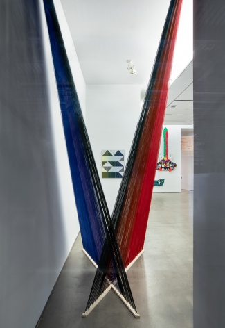 Installation view of "Adriadne Unraveling". Textile works are hung on the wall. An installation hangs in an "X" in the foreground.