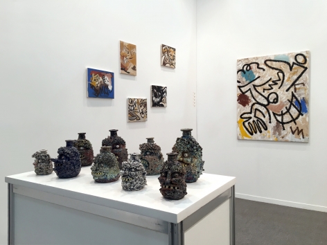 Installation view of the art fair booth at Zona Maco. Paintings are on the walls and sculptures are on a table