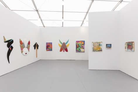 Installation of an art fair booth, showcasing paintings and flat sculptures on the walls