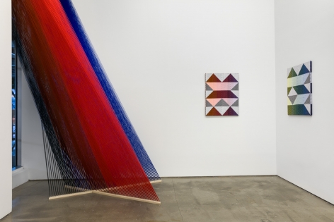 Installation view of "Adriadne Unraveling". Textile works are hung on the wall. A large string installation in the left corner