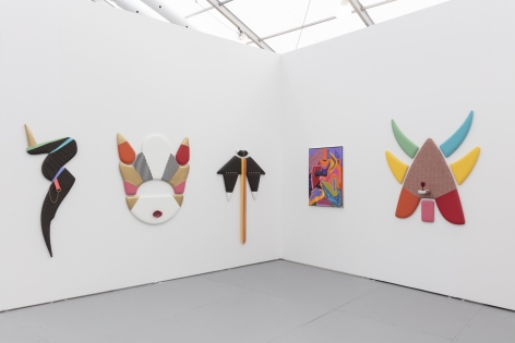Installation view of an art fair booth, showcasing paintings and flat sculptures on the walls